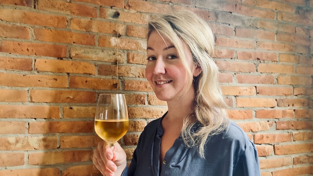 woman holding a glass of white wine with a brick wall in the background